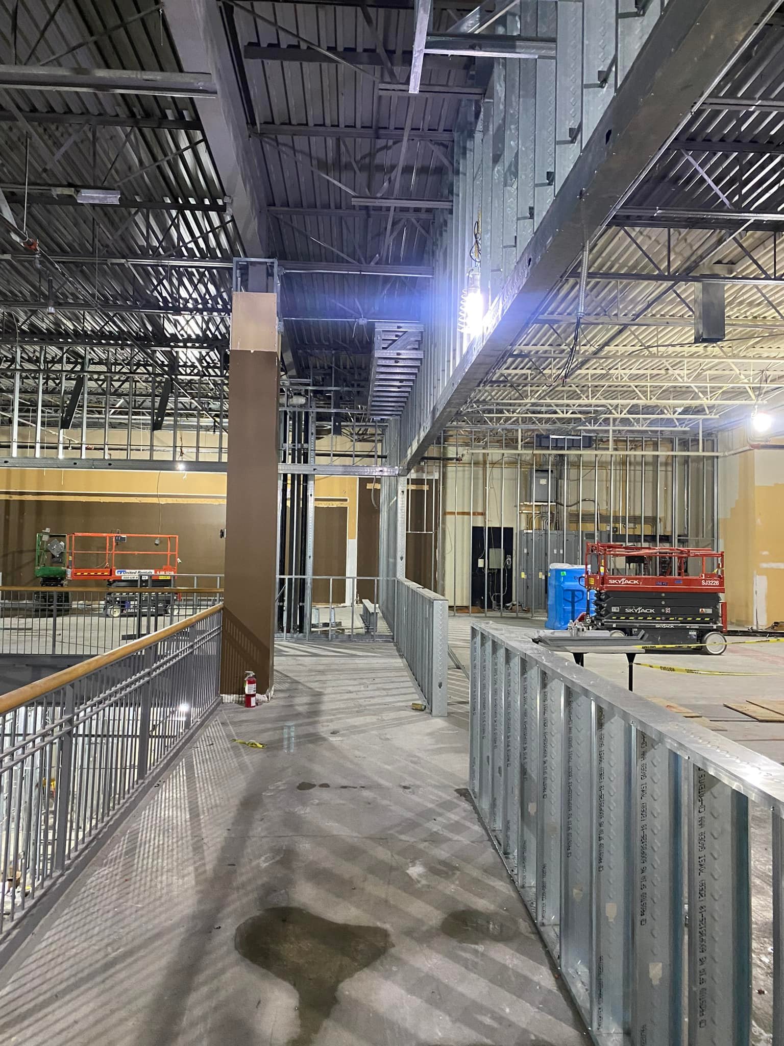 Retail construction interior with steel stud framing, mezzanine walkway, and ceiling infrastructure in progress